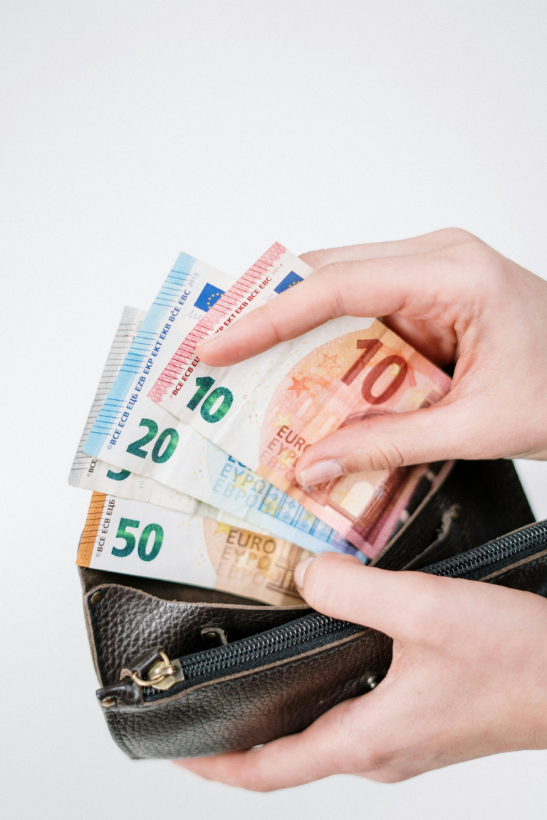 Person hält eine geöffnete Geldbörse in den Händen, aus denen Geldscheine herausschauen.